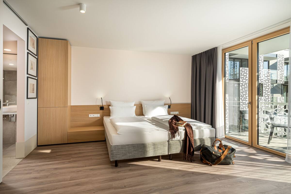 A modern hotel room with a large bed, a wardrobe, a bathroom, and a balcony with a city view.