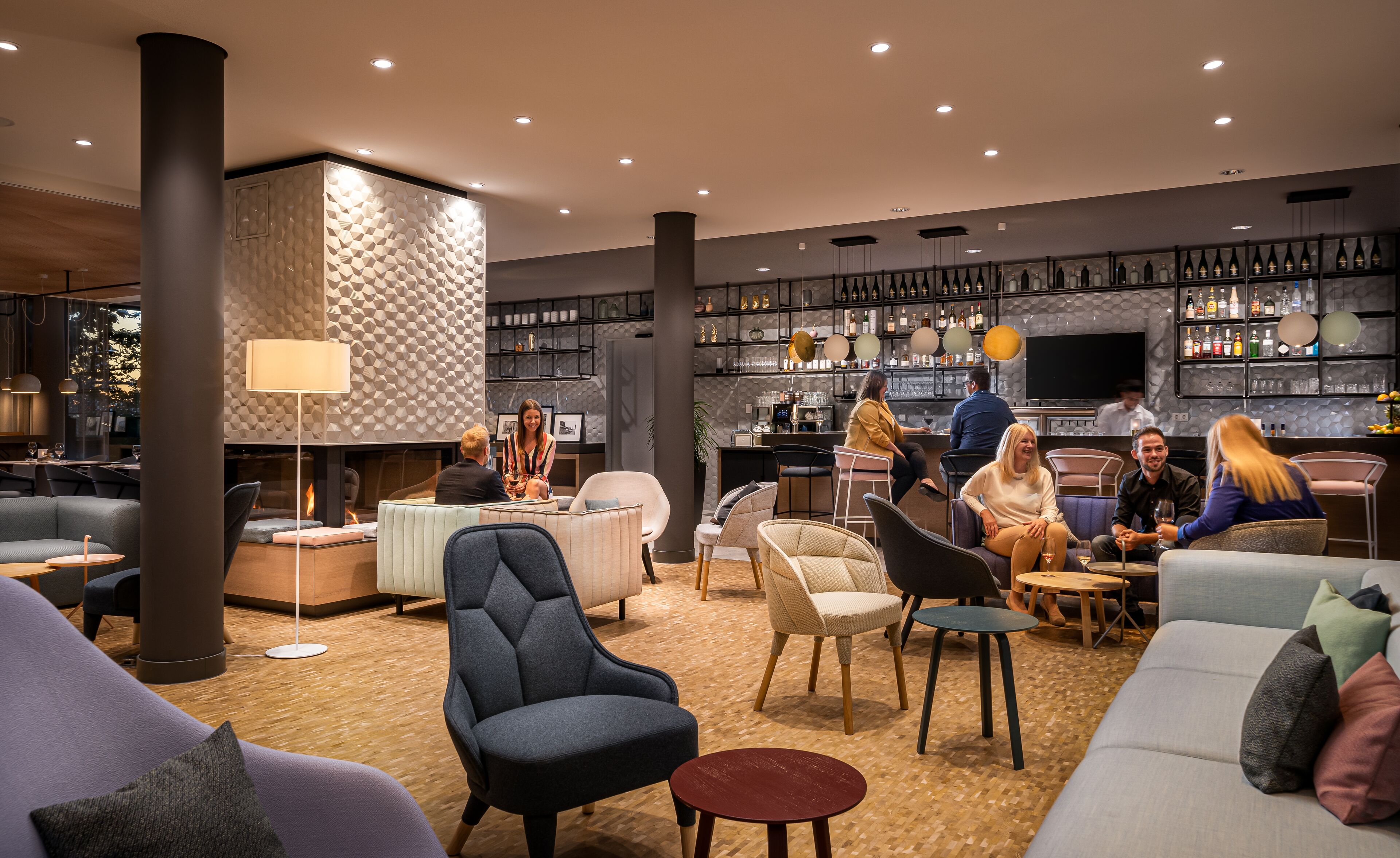 A modern lounge area with seating, a fireplace, and a bar with shelves of bottles.