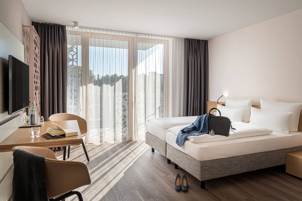A modern hotel room with a bed, a desk, a chair, and a TV.