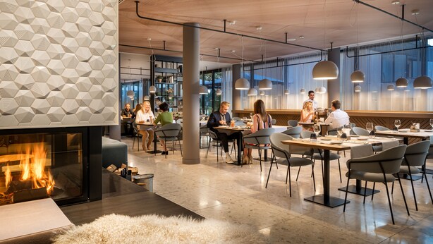 A modern restaurant with a geometric wall pattern, a fireplace, and contemporary lighting.