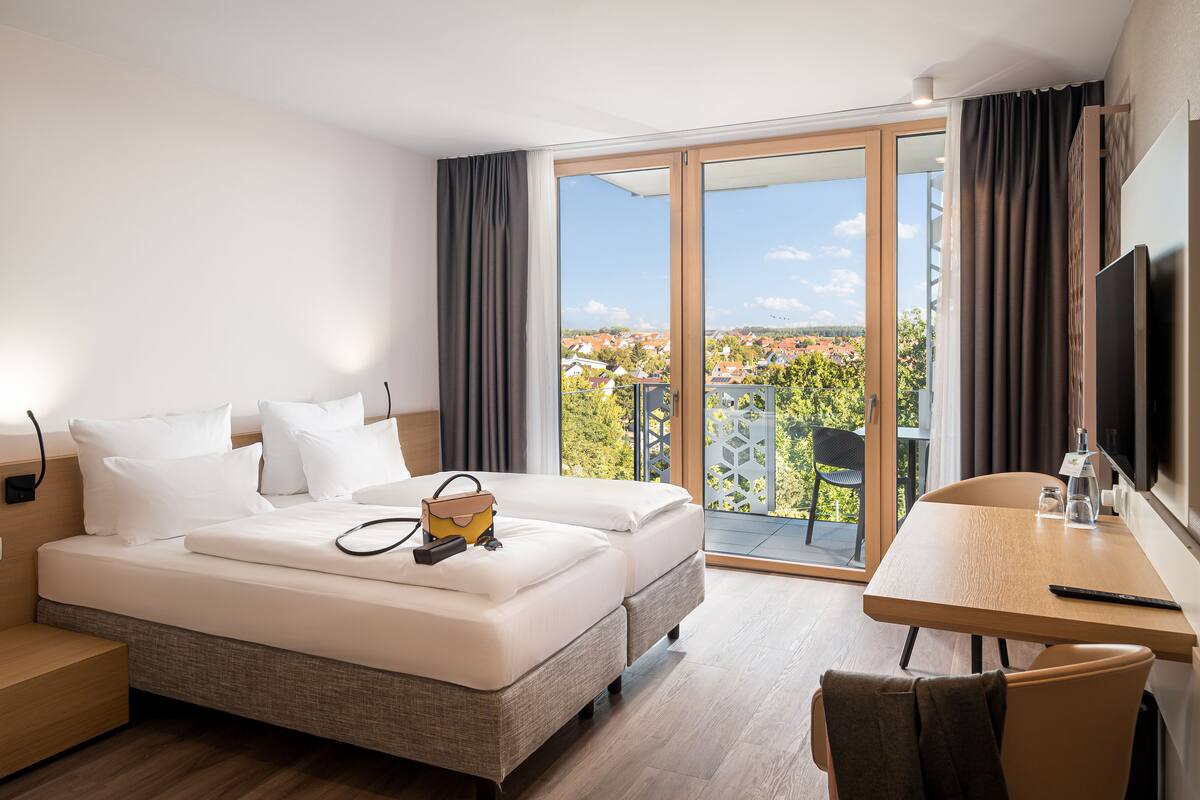 A hotel room with a bed, bedside table, and a balcony with a view.