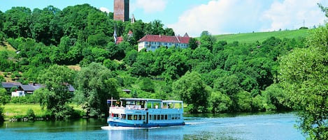 A river with a boat, surrounded by lush greenery and a castle-like structure in the background.