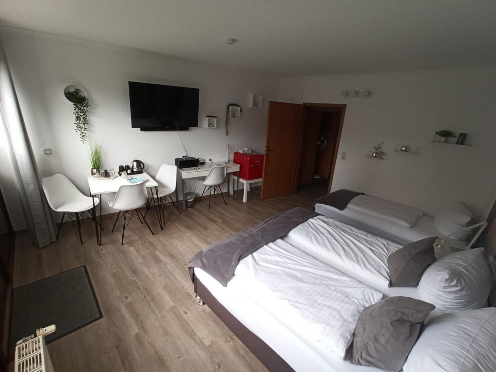 Habitación de hotel moderna con una cama grande, un escritorio con sillas, un televisor de pantalla plana y una planta pequeña.