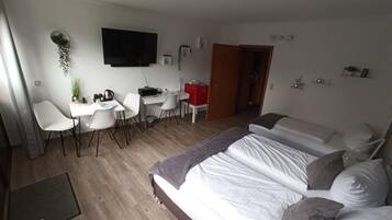 Habitación de hotel moderna con una cama grande, un escritorio con sillas, un televisor de pantalla plana y una planta pequeña.