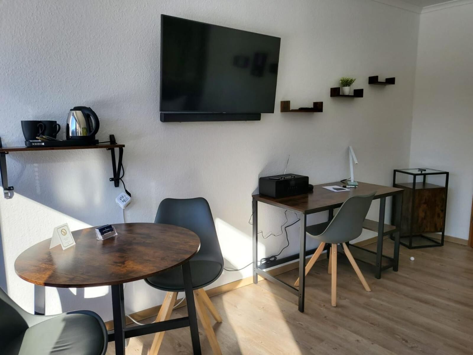 Un soggiorno moderno con una TV a schermo piatto, un tavolino da caffè, due poltrone, una scrivania con un computer e un comodino con una lampada.