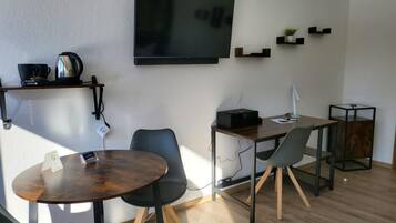 Un soggiorno moderno con una TV a schermo piatto, un tavolino da caffè, due poltrone, una scrivania con un computer e un comodino con una lampada.
