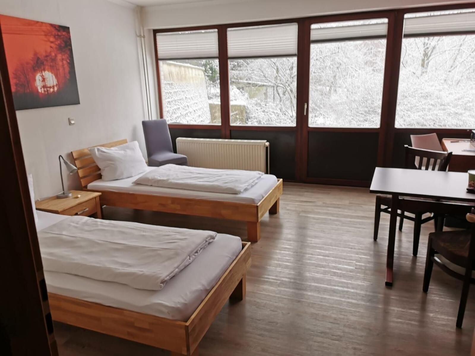 A hotel room with two wooden beds, a desk, a chair, and a large window with a view of snow-covered trees.