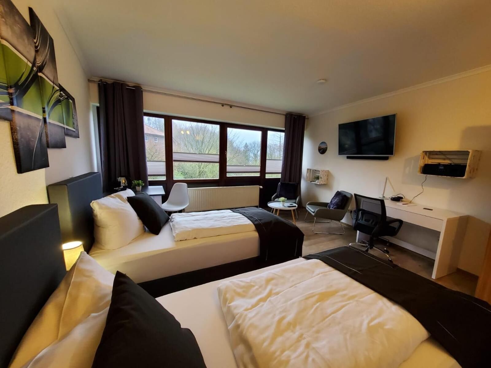 A hotel room with two beds, a desk, a chair, a TV, and large windows.