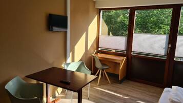 A compact room with a wooden desk, a green chair, a small table, and a bed.