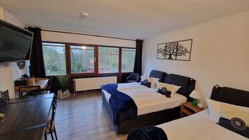 Een hotelkamer met een groot bed, een bureau en een raam met uitzicht op bomen.