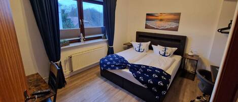 A bedroom with a bed, a window with curtains, a painting on the wall, and a radiator.