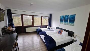 A hotel room with two beds, a desk, and a window with a view of trees.