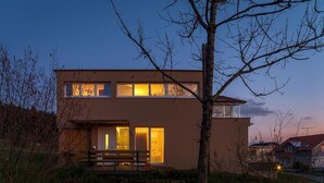 Una casa moderna de dos pisos con techo plano, ventanas grandes y una puerta principal visible.