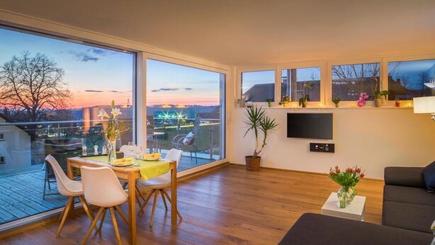 Ein modernes Wohnzimmer mit Essbereich, großen Fenstern, einem Flachbildfernseher und einem Balkon mit Aussicht.