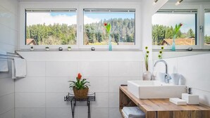 Ein modernes Badezimmer mit großem Fenster, Waschbecken, Spiegel und Holzwaschtisch.