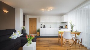 Ein modernes Wohnzimmer mit einer schwarzen Couch, einem weißen Couchtisch und einem Essbereich mit Holztisch und Stühlen.