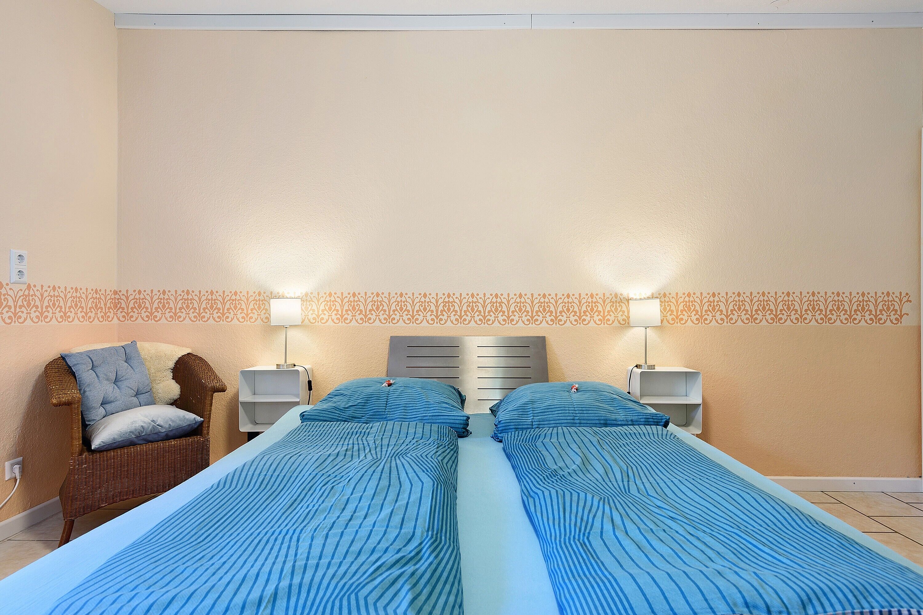 Een tweepersoonskamer met twee bedden, een stoel, nachtkastjes en een behang met patroon.