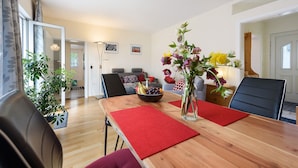 Ein Essbereich mit einem Holztisch, roten Platzsets, einer Vase mit Blumen und einer Obstschale.
