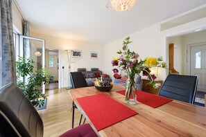 A dining area with a wooden table, red placemats, a vase with flowers, and a bowl of fruit.