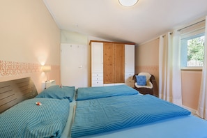 A bedroom with two beds, a wardrobe, a bedside table, and a window with curtains.