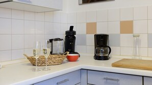 Eine Küche mit weißen Fliesen, einer Kaffeemaschine, einem Korb und zwei Gläsern.