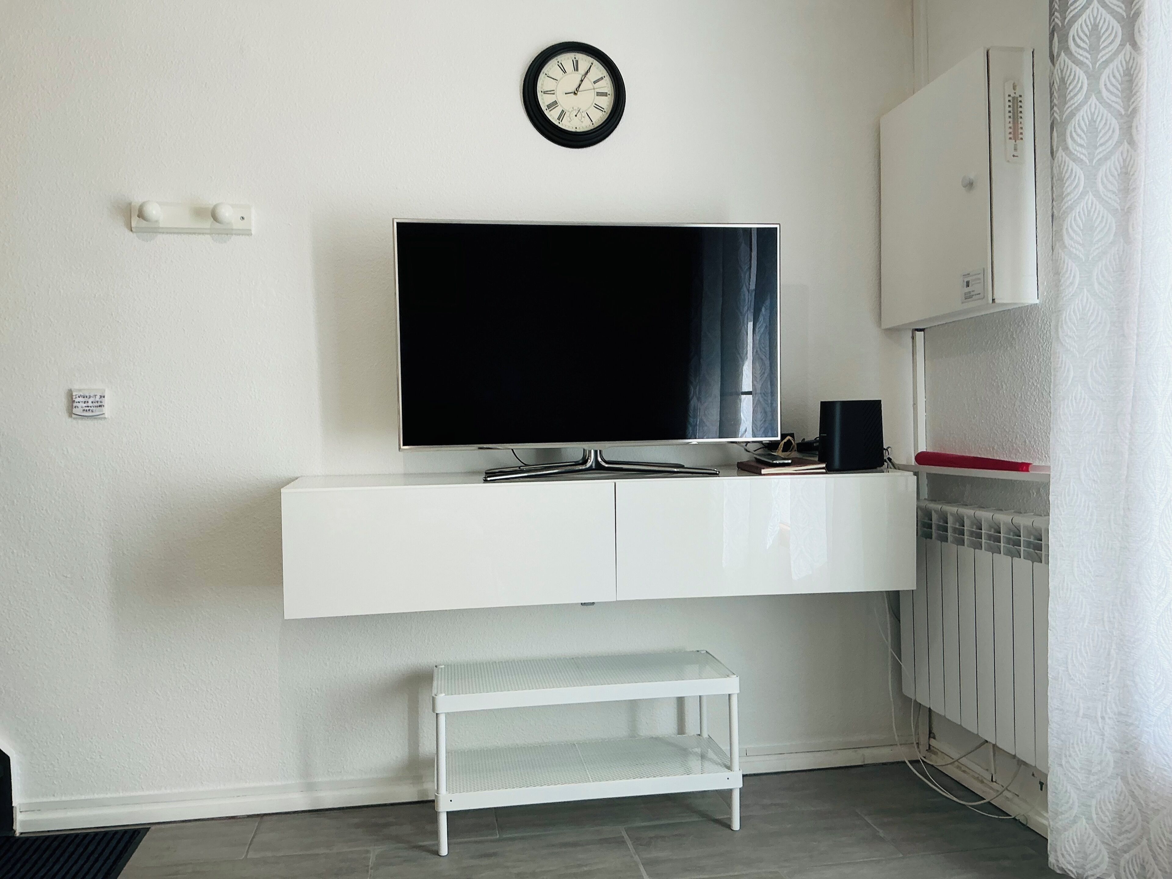 Una sala de estar moderna con televisor de pantalla plana, muebles blancos, un pequeño banco y un radiador.