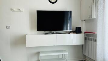 Una sala de estar moderna con televisor de pantalla plana, muebles blancos, un pequeño banco y un radiador.