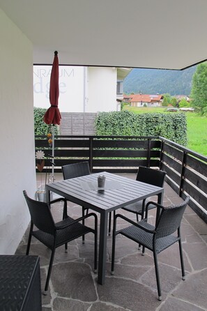 Eine Terrasse im Freien mit Tisch und Stühlen, einem roten Sonnenschirm und Blick auf einen Berg.