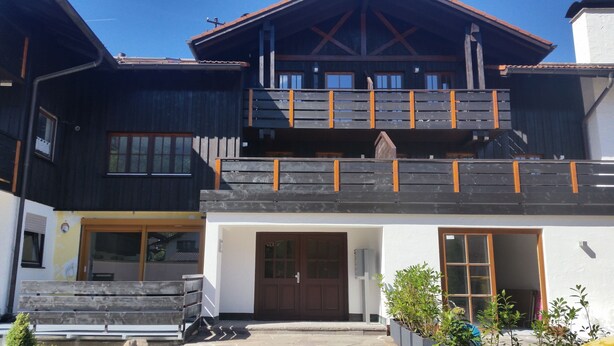 A two-story building with a wooden balcony, a large window, and a door. - Quietly located vacation apartment in Pfronten (Pfronten)