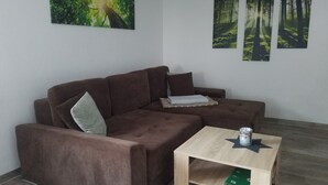 A living room with a brown sectional sofa, a small wooden coffee table, and three forest-themed wall art pieces. - Quietly located vacation apartment in Pfronten (Pfronten)