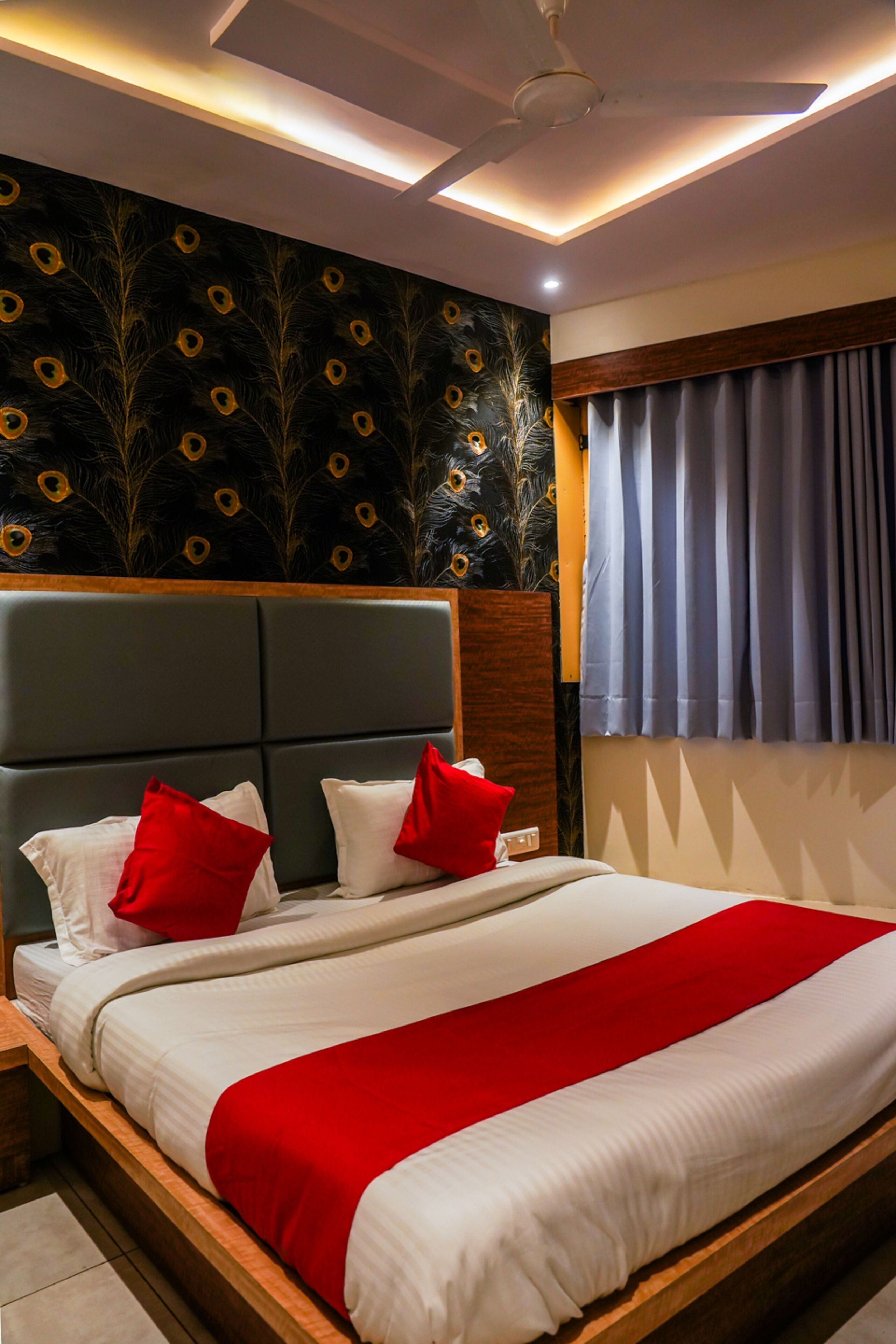 Ett hotellrum med en stor säng, en sänggavel med ett påfågelsfjädersmönster, rött och vitt sänglinne och en takfläkt.