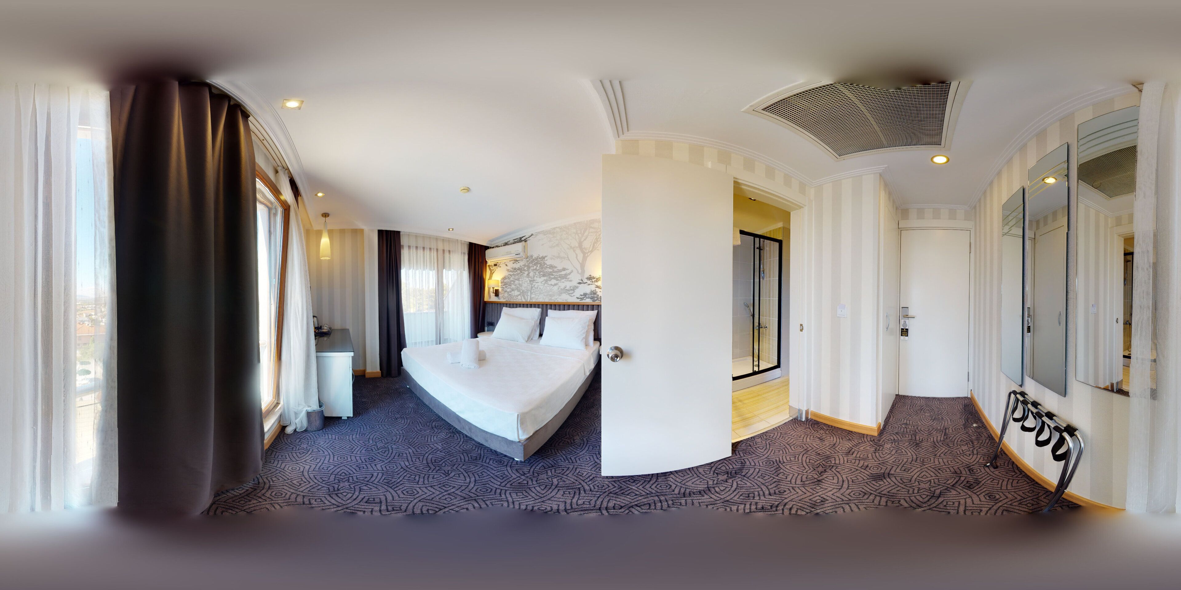A hotel room with a large bed, a desk, a shower, and a view of the city.