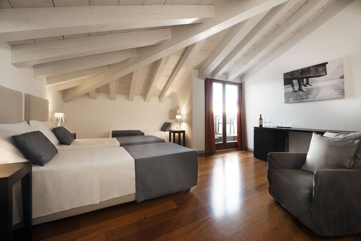 A modern bedroom with a loft-style ceiling, a large bed, a sofa, and a desk area.