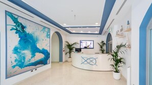 A reception area with a large abstract painting, a reception desk, and potted plants. - Hotel del Porto (Torri del Benaco)