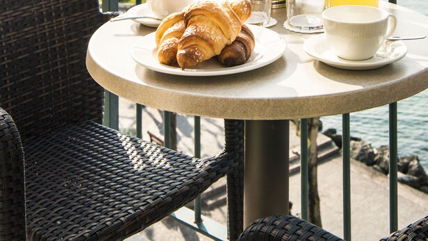 A table with croissants, fruit, and a pitcher of orange juice on a balcony overlooking the sea. - Hotel del Porto (Torri del Benaco)