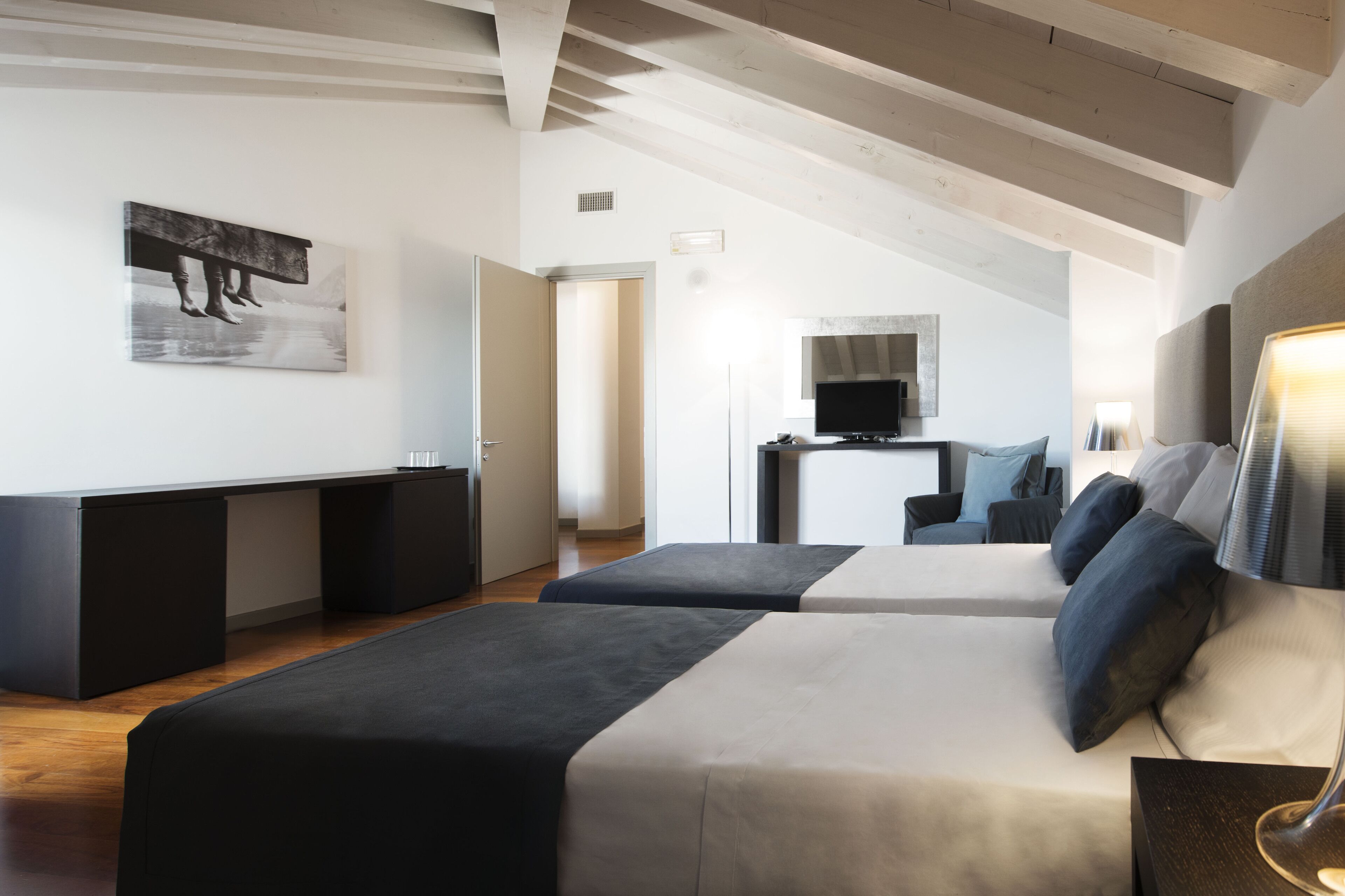 A modern bedroom with two beds, a TV, and a desk.