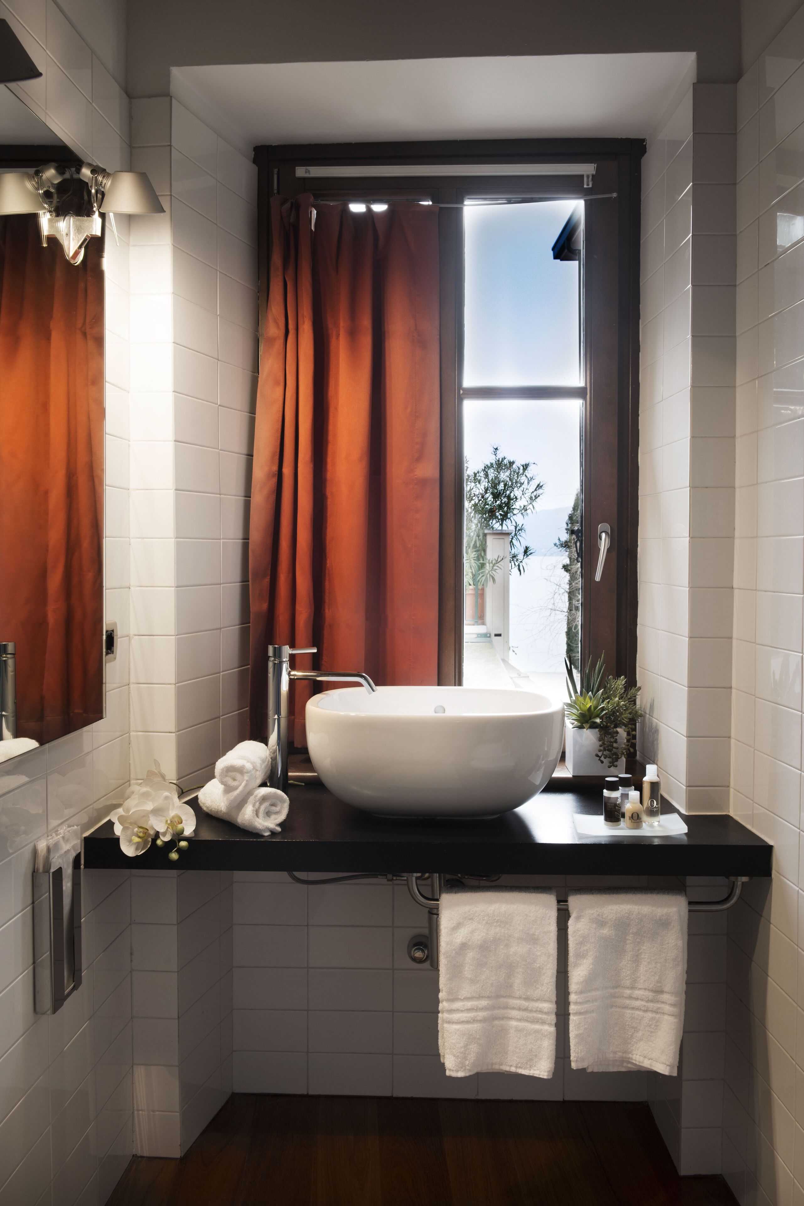 Un baño moderno con un lavamanos grande y blanco, una ventana con cortinas marrones y vistas al exterior de zonas verdes.
