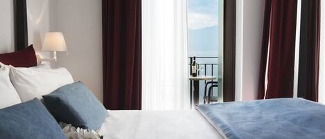 Habitación de hotel con cama, mesita de noche, lámpara, vistas al exterior y un balcón con mesa y sillas.