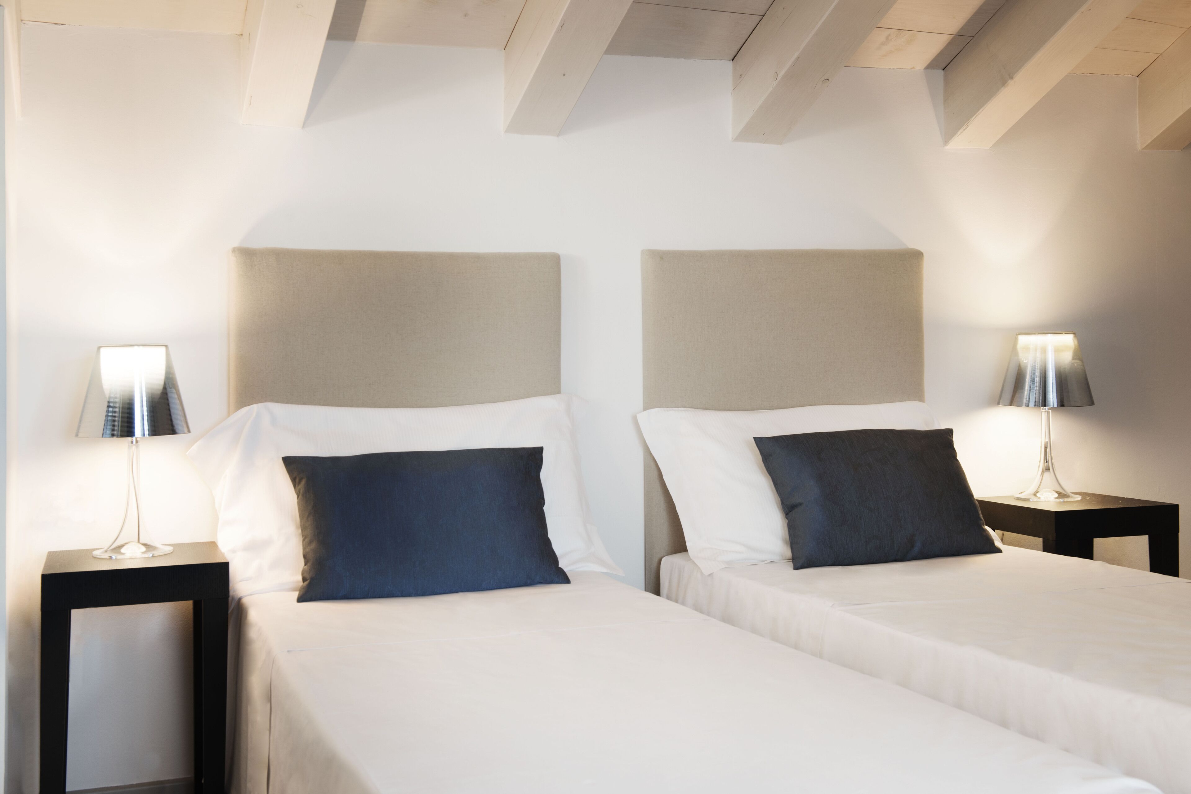 Habitación de hotel con dos camas, cada una con cabecera, mesitas de noche y lámparas.