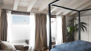 A bedroom with a bed, a chair, a potted plant, and a view of a tower through sheer curtains. - Hotel del Porto (Torri del Benaco)