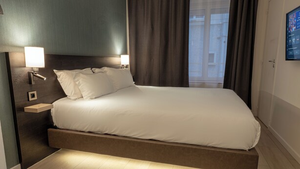 A modern hotel room with a bed, bedside lamps, a nightstand, and a view of the outside. - Five Resort Cholet Centre (Cholet)