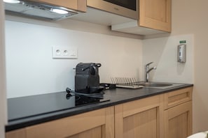 A kitchen with a black countertop, a coffee maker, a sink, wooden cabinets, and a microwave. - Five Resort Cholet Centre (Cholet)