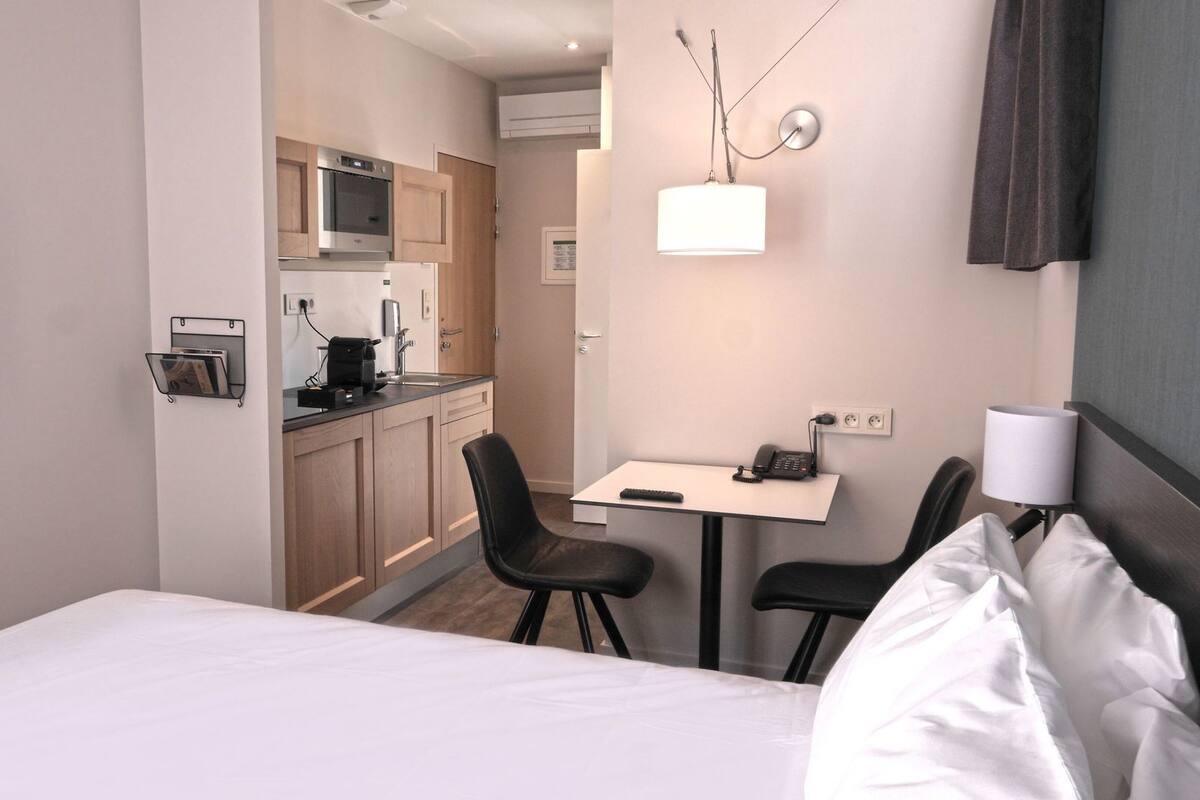 Une chambre d’hôtel équipée d’un lit, d’un bureau avec une chaise, d’une kitchenette et d’un téléviseur fixé au mur.
