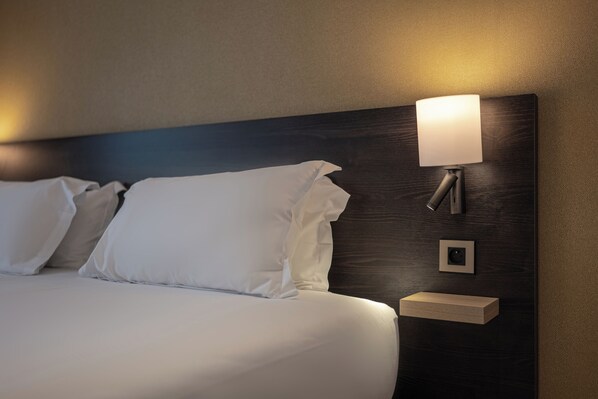 A neatly made bed with white linens, a wall-mounted bedside table, and a wall-mounted lamp.
