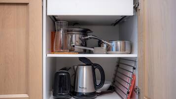 A kitchen cabinet with a coffee maker, kettle, and pots on the shelves.