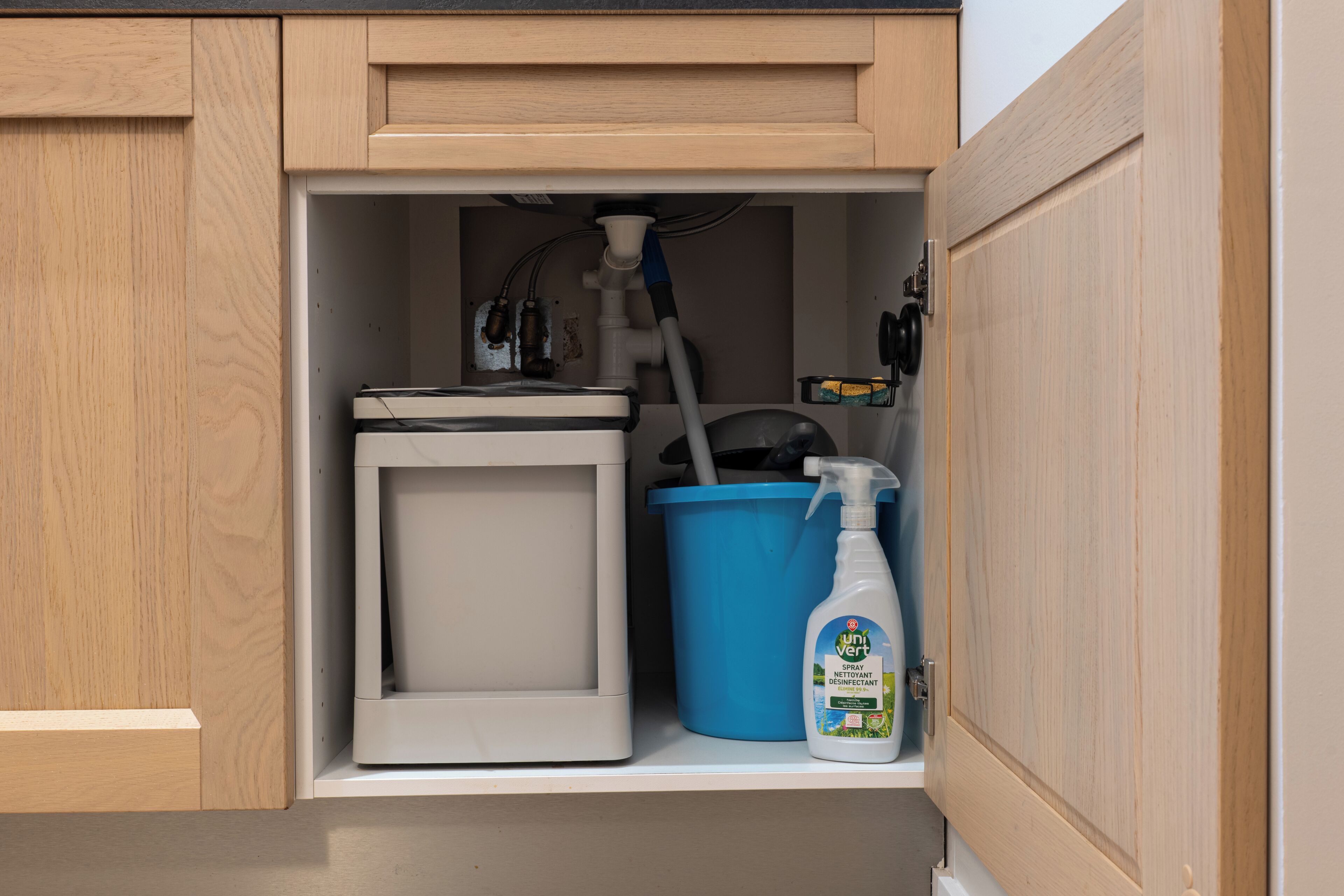 Un baño con un inodoro, un cubo azul y una botella pulverizadora.