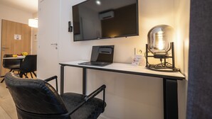 A modern room with a flat-screen TV mounted on the wall, a laptop on a desk, a vintage-style lamp, and a dining area with chairs and a table. - Five Resort Cholet Centre (Cholet)