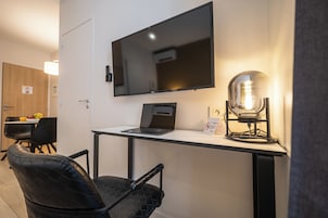 Une chambre moderne dotée d’un téléviseur à écran plat fixé au mur, d’un ordinateur portable posé sur un bureau, d’une lampe de style rétro et d’un coin repas avec des chaises et une table.