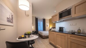 A modern hotel room with a kitchenette, a bed, a dining area, and a view of the cityscape. - Five Resort Cholet Centre (Cholet)