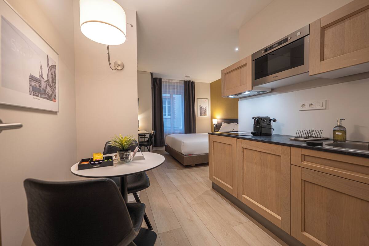 Une chambre d’hôtel moderne dotée d’une kitchenette, d’un lit, d’un coin repas et offrant une vue sur le paysage urbain.